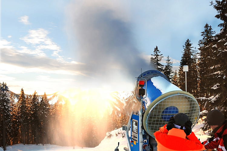 Two people working with a snow-making machine launch it towards the ski slope.