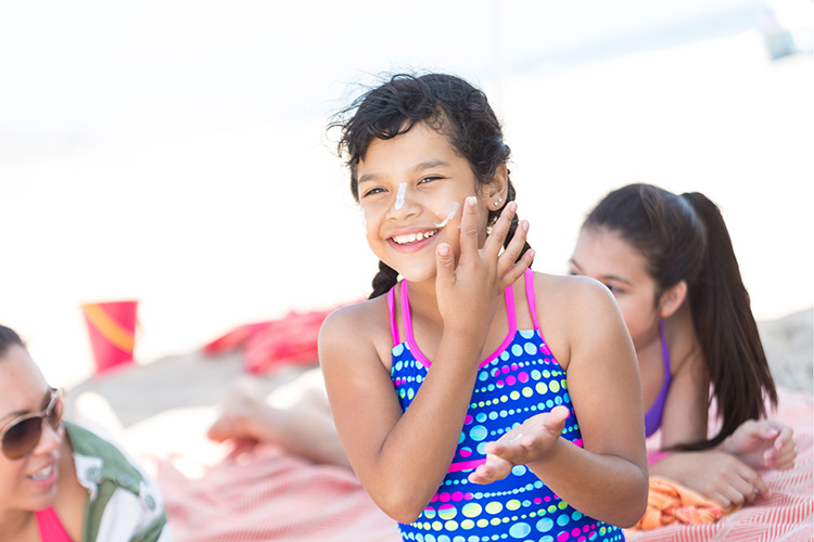 A girl applies sunscreen onto her face on the beach.