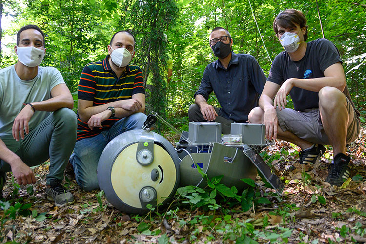 Four people standing next to a sloth-like robot