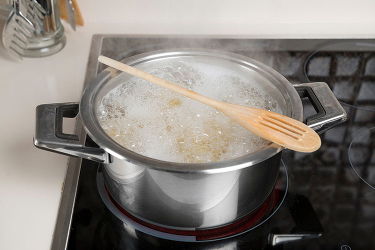 A pot with boiling water and pasta, and a wooden spoon on top