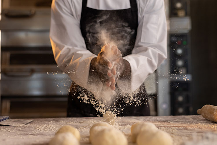 Image of a baker with flour on their hands while working with dough