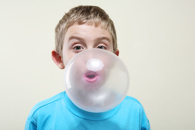 Image of a kid blowing a large bubble with pink gum