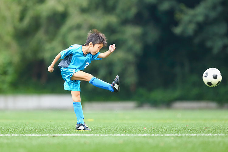 Image of a kid kicking a soccer ball on the field during a game